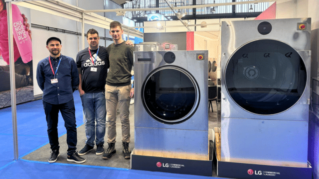 LG Commercial Laundry exhibition stand at GAST Ljubljana showcasing professional washers, dryers, and finishing equipment, with team members and visitors engaging in technical discussions.